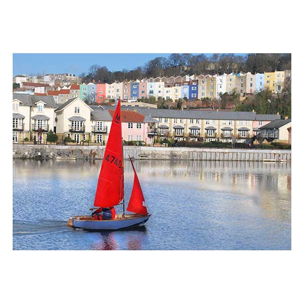 Boat with red sailes in water houses in background