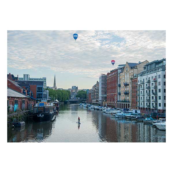 Paddleboarder on water under sky of balloons